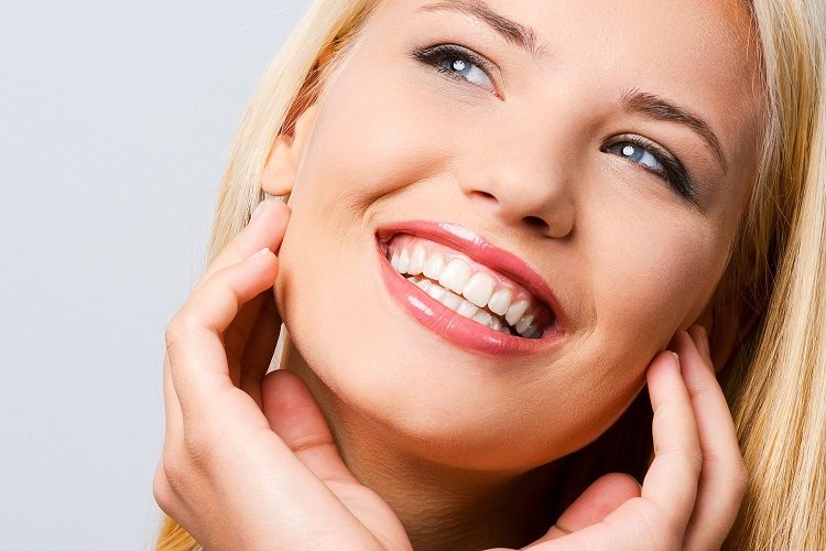 blonde woman smiles while holding her cheeks